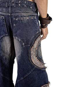 Close-up of washed denim showing the rear pocket, curved panel construction, exposed seams and distressed raw edges.